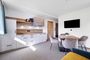 A modern kitchen with a built-in oven, a dining area with a wooden table and chairs, and a flat-screen TV mounted on the wall.