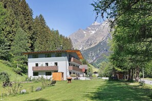 A modern multi-story building with balconies, surrounded by lush greenery and mountains in the background.