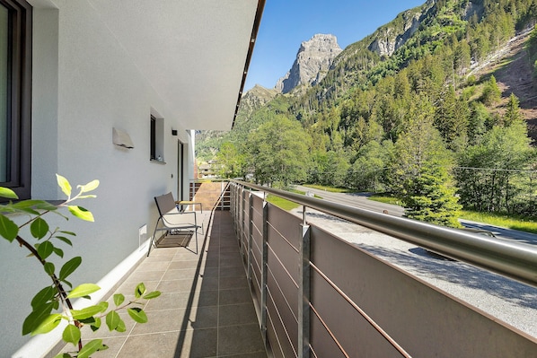 A balcony with a view of a mountain, a chair, and a railing.