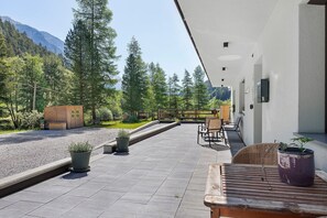 Une terrasse avec des sièges extérieurs, des plantes en pot et une vue sur une zone boisée, avec des montagnes en arrière-plan.