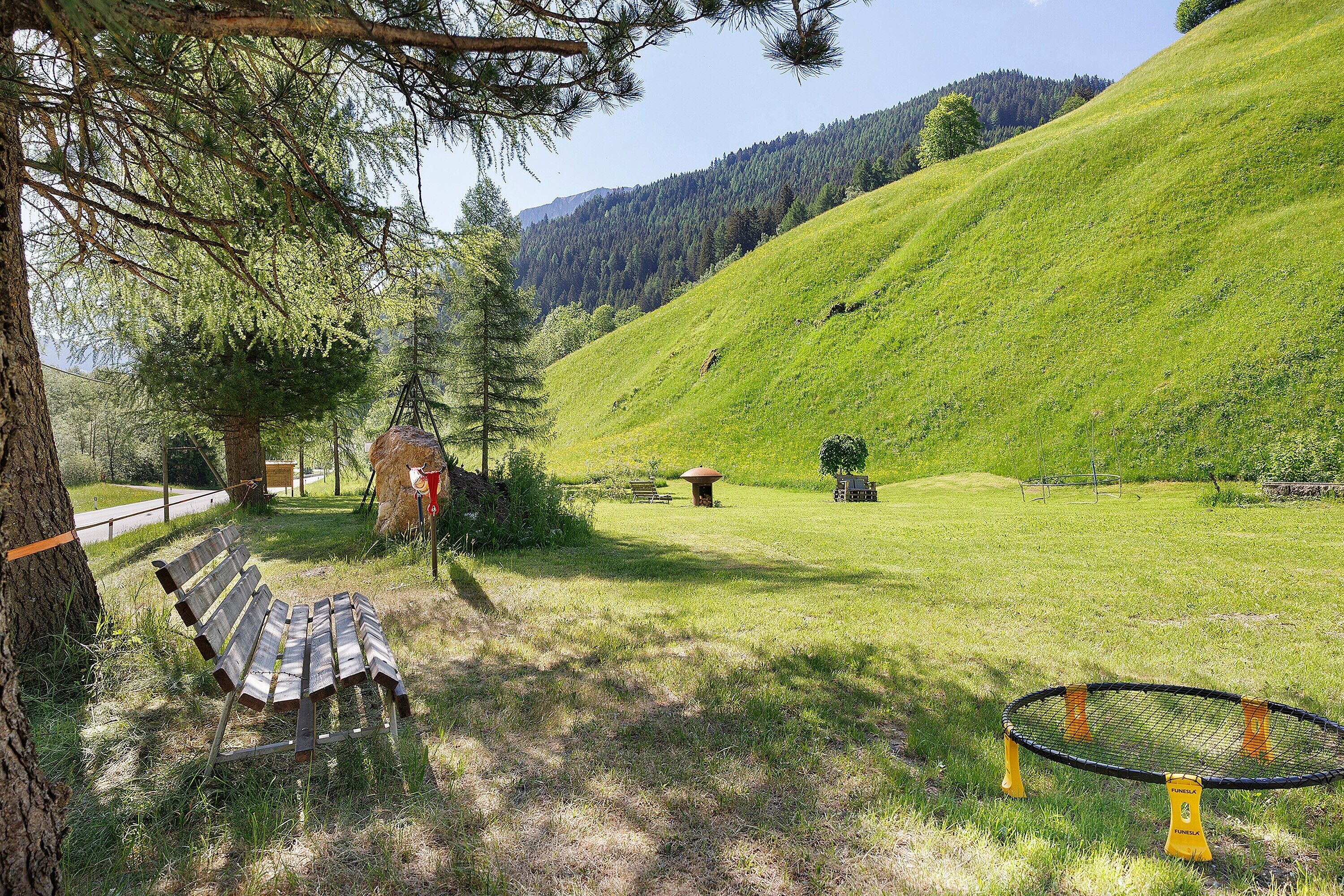 A grassy outdoor area with a bench, a trampoline, and a picnic table.