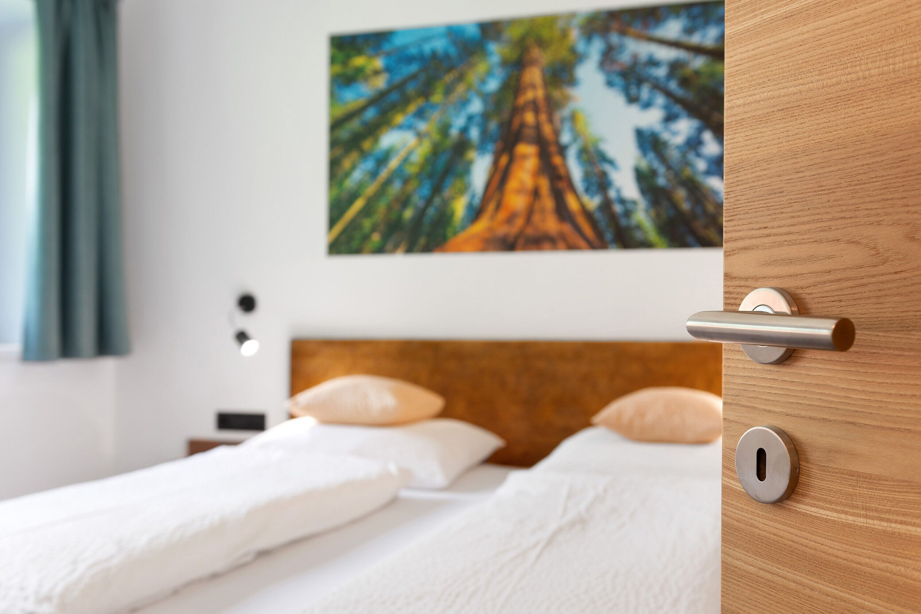 Ein Hotelzimmer mit einem hölzernen Kopfteil, einem Bett mit weißer Bettwäsche und einem Baumgemälde an der Wand.