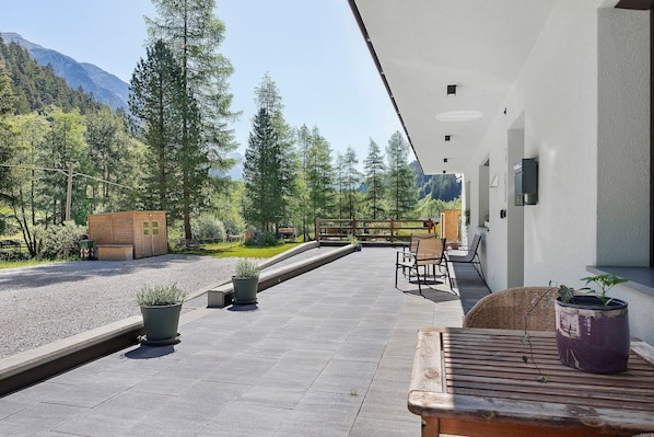 A patio with outdoor seating, potted plants, and a view of a forested area with mountains in the background.
