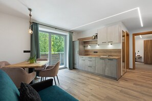 A modern kitchen with wooden cabinets, a dining area with a table and chairs, and a view of greenery outside.