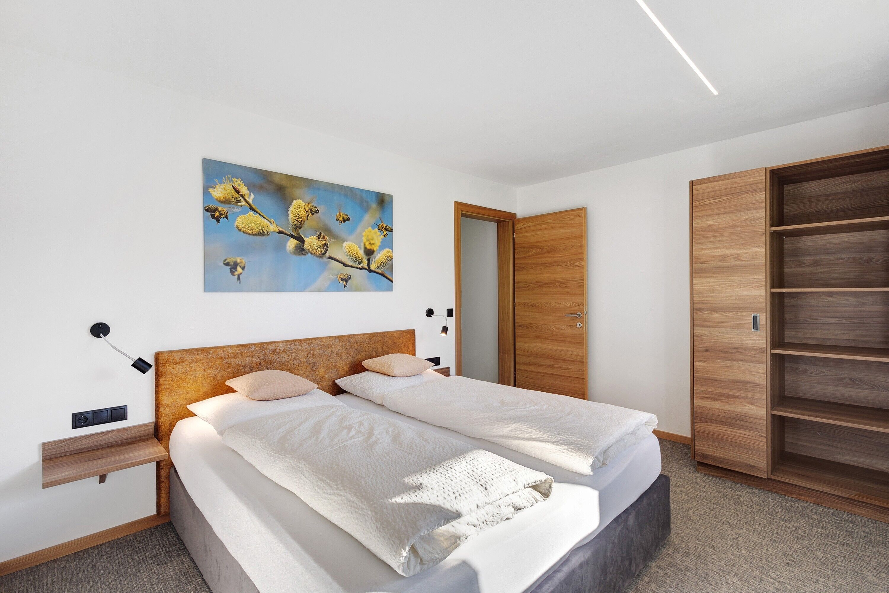 Une chambre à coucher comprenant un lit, une armoire en bois, une étagère fixée au mur, un tableau et une table de chevet.