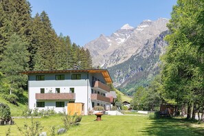 A modern multi-story building with balconies, surrounded by lush greenery and mountains in the background.
