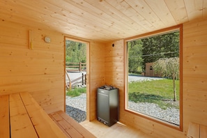 A wooden cabin interior with a sauna, large windows, and a view of the outdoors.