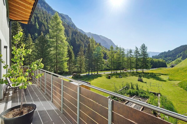 A balcony with a potted plant, a metal railing, and a view of a mountainous landscape.
