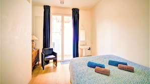 Ein Hotelzimmer mit Bett, Stuhl, Schreibtisch, Lampe und einem fensterbepflanzten Fenster.