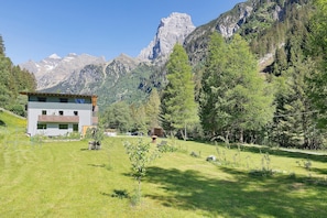 A building with a sloped roof, a grassy yard, and a mountainous backdrop. - Apartment Nature House Mushrooms – Peaceful Retreats in the Mountains (Brennero)