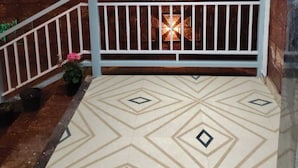 A covered outdoor area with a patterned floor, a white railing, and a window with curtains.