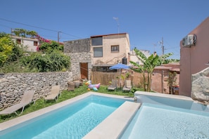 A swimming pool with lounge chairs, a stone wall, and a building with a red roof. - Country House 'Kourtsa Traditional Home with Pool' with Mountain View, Wi-Fi and Air Conditioning (Vafes)