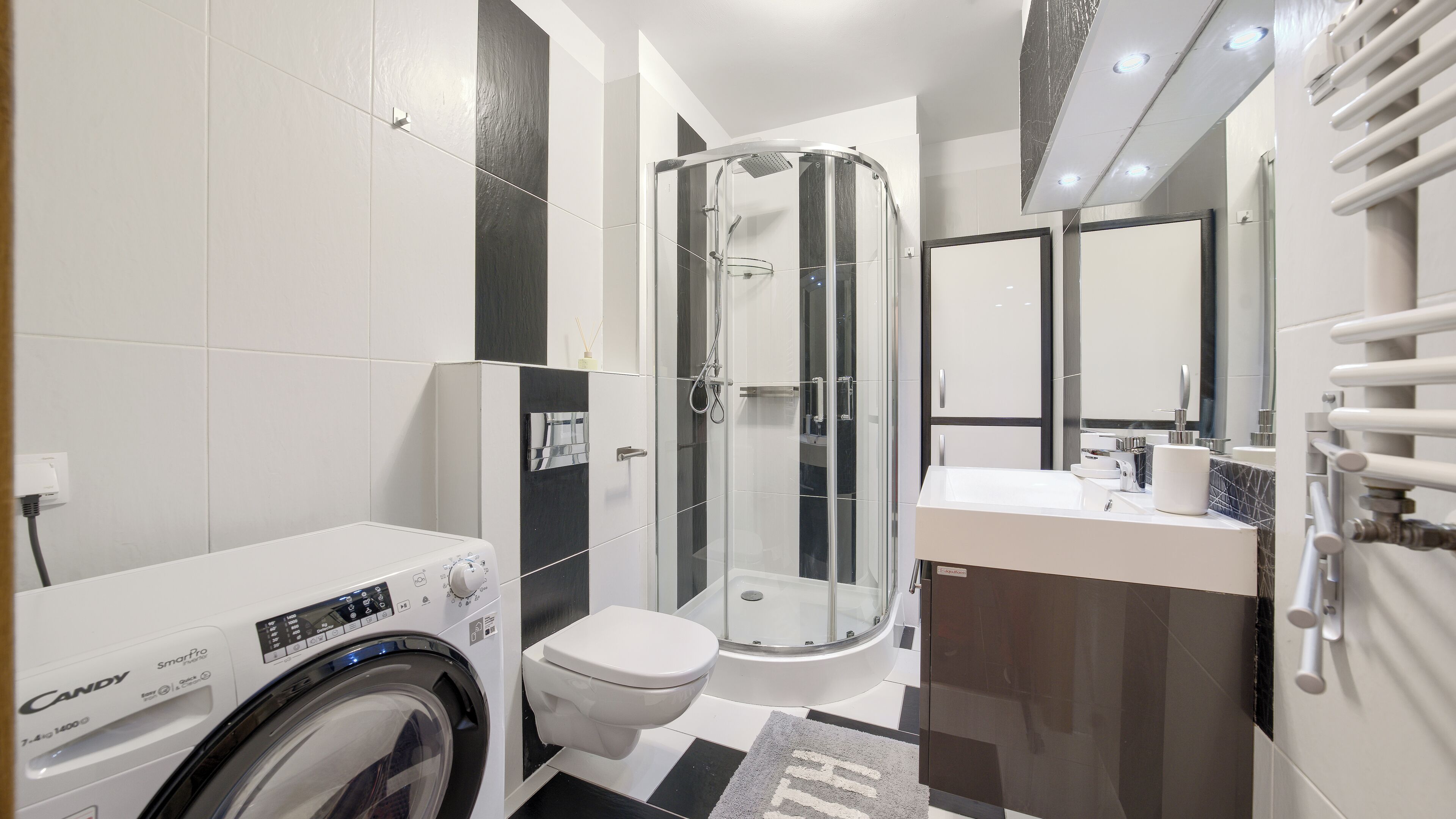 Een moderne badkamer met een wasmachine, toilet, douche en een wastafel.