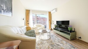 A living room with a sofa, a TV, a coffee table, and a view of a building through the window.