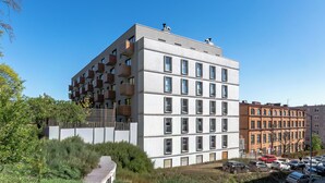 A multi-story building with balconies, a parking lot, and adjacent older buildings.