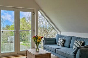 Ein Zimmer mit einem blauen Sofa, einem Holztisch und einer Blumenvase.