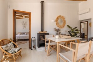 Ein gemütliches Zimmer mit einem Holzesstisch, Stühlen, einem Korbstuhl, einem wandmontierten Spiegel, einem dekorativen Kranz und einem Kamin mit dem Schriftzug 'NAMASTE'.