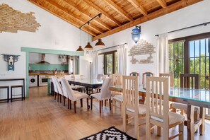 Uma sala de jantar espaçosa com mesa de vidro, cadeiras de madeira e iluminação pendente.