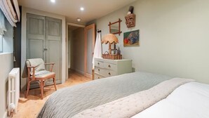 Un dormitorio con cama, una silla, un tocador, una lámpara y una puerta.