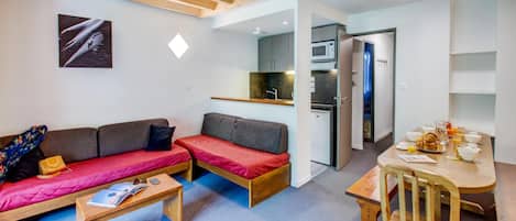Un espacio habitable compacto con sofá, una mesita, kitchenette y zona de comedor.