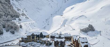 Un centro turístico en la montaña cubierto de nieve, con varios edificios, una zona de estacionamiento y pistas de esquí.