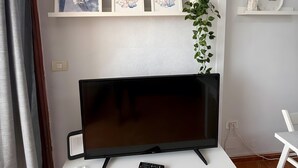Una TV a schermo piatto su un mobile bianco, un'opera d'arte appesa al muro e una sveglia su uno scaffale.