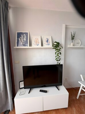 Et fladskærms-TV på et hvidt skab, billedkunst på væggen og et ur på en hylde.