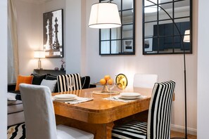 A dining area with a wooden table, striped chairs, a lamp, and a chess-themed painting. - Angelico apt with terrace and lift (Firenze)