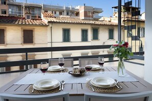A table set for a meal with wine glasses, plates, and a vase of flowers on a balcony overlooking buildings. - Angelico apt with terrace and lift (Firenze)
