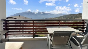 A balcony with a table and chairs, overlooking a mountain range with snow-capped peaks and a clear blue sky. - Montana Alpine Outlook 4 Pax Panoramic Alps View (Crans-Montana)