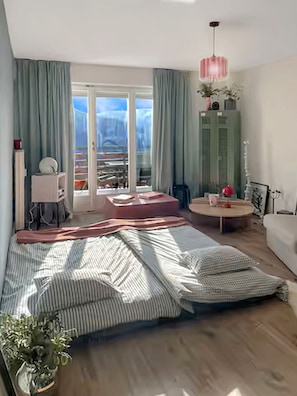 Ein Schlafzimmer mit einem Bett, einem runden Tisch, einem Stuhl, einer Topfpflanze und Blick durch eine Glastür.