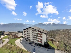 Ein mehrstöckiges Gebäude mit Balkonen, einem Parkplatz und Blick auf Berge.
