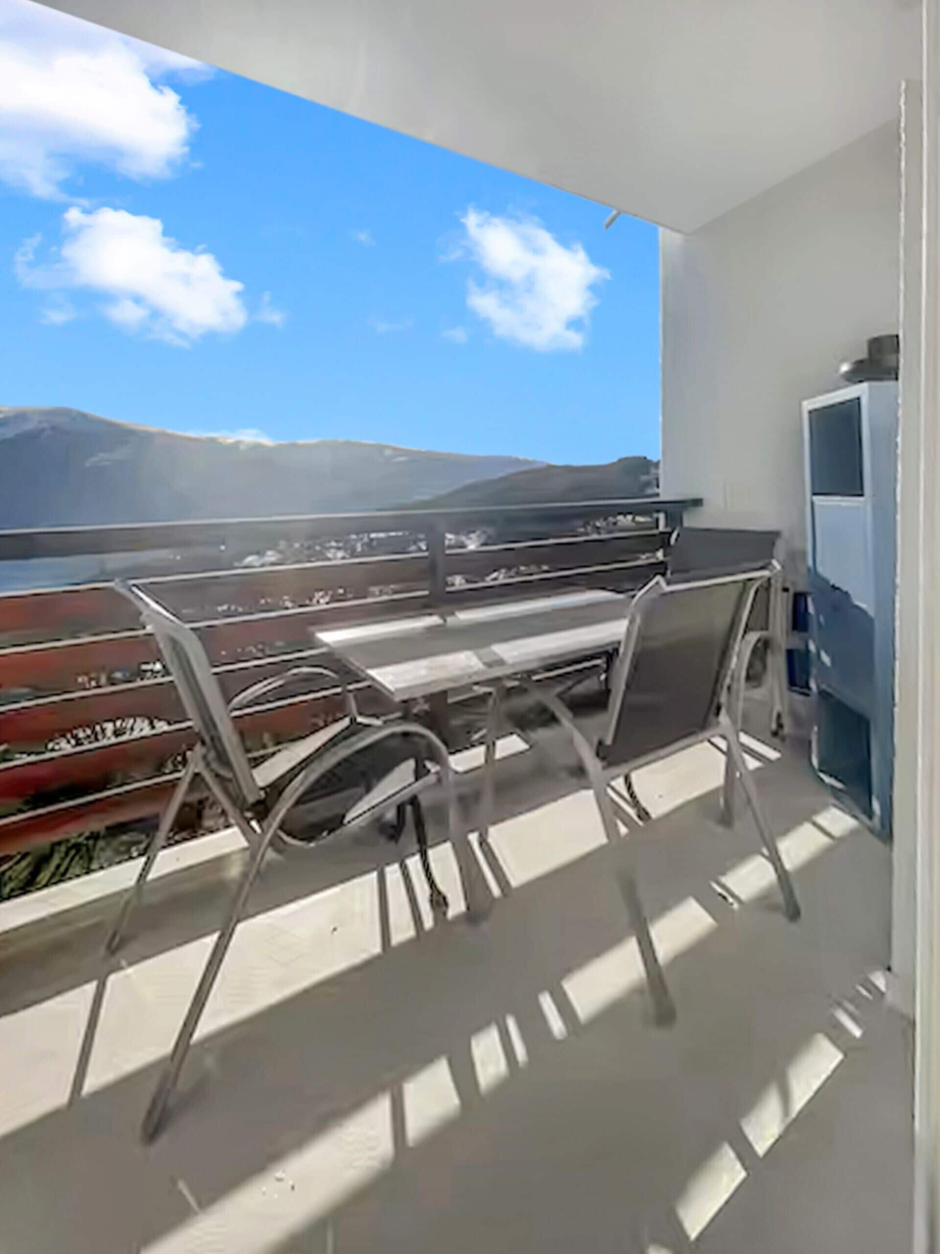 Un balcon avec une table et des chaises, un téléviseur et une vue sur une montagne.