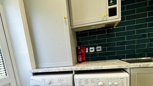 A laundry area with two washing machines, a fire extinguisher, and a tiled backsplash. - House Sleeps 6 Garden (Mitcham)