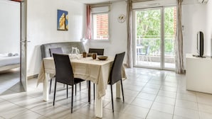 Uma sala de jantar com mesa posta para quatro pessoas, sofá, TV e varanda com vista.