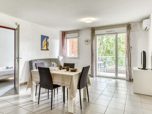 A dining area with a table set for four, a sofa, a TV, and a balcony with a view. - Chic 4-guest Studio, Wellness & Pool (Argelès-sur-Mer)