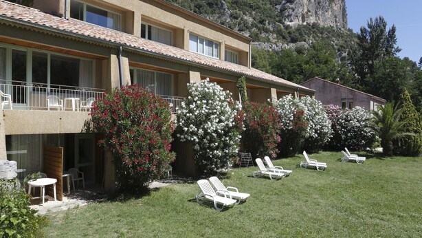A two-story building with a balcony, white lounge chairs, and a garden with flowering bushes. - Nature Studio for 4 in Chames (Vallon-Pont-d'Arc)