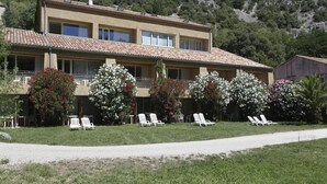 A two-story building with a tiled roof, a balcony, and white lounge chairs in front. - Nature Studio for 4 in Chames (Vallon-Pont-d'Arc)