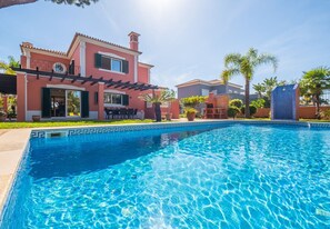Ein Pool mit Pergola, ein rotes Gebäude und Palmen.