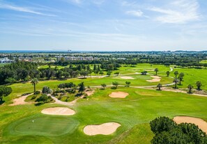 Ein Golfplatz mit Sandbunkern, Bäumen und einer entfernten Skyline.