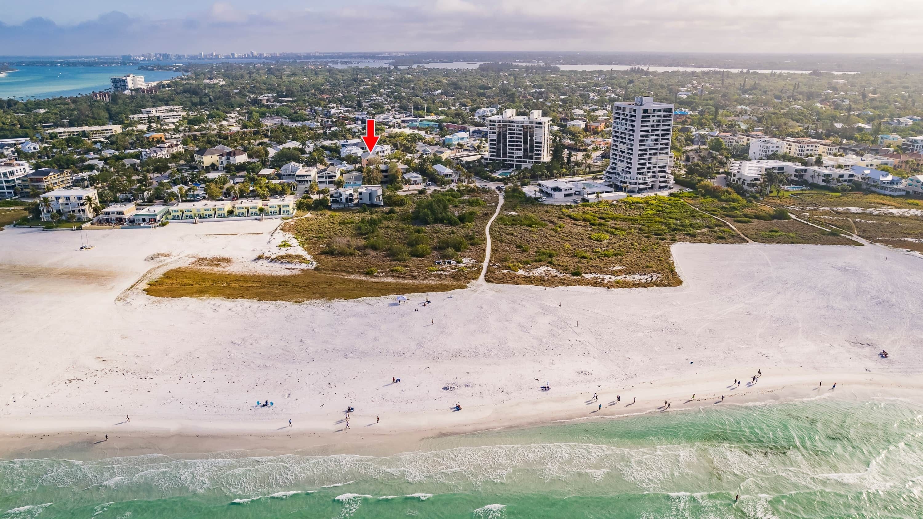 An aerial view of a coastal area with a beach, buildings, and a road.