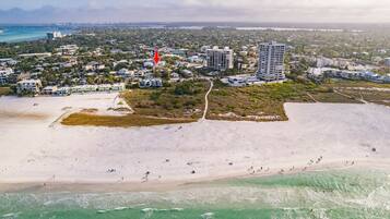 An aerial view of a coastal area with a beach, buildings, and a road.