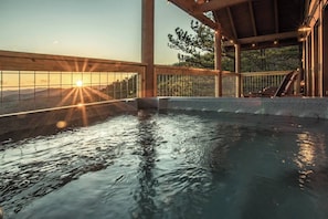Ein Whirlpoolbereich mit Blick auf den Sonnenuntergang, eine Holzterrasse und eine überdachte Sitzgruppe.