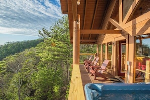 Eine Holzterrasse mit Liegestühlen und einem Whirlpool mit Blick auf einen bewaldeten Bereich.