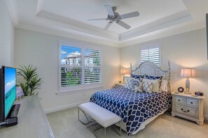 A bedroom with a bed, a bench, a nightstand, a TV, and a ceiling fan. - Talis Park at Carrara - FULL GOLF TRANSFER AVAILABLE (Naples)