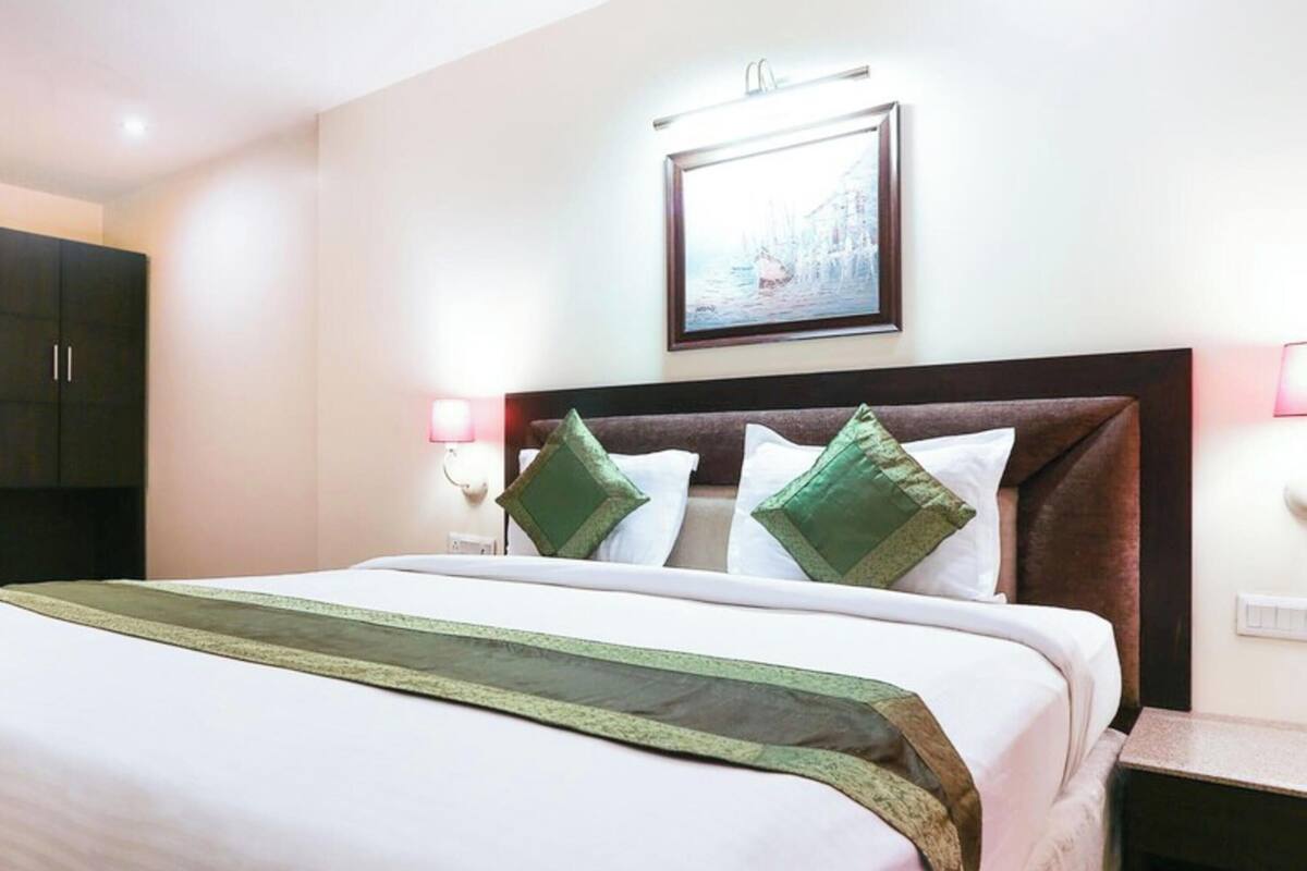 Quarto de hotel com uma cama, um guarda-roupa, um quadro na parede e uma mesa de cabeceira com abajur.