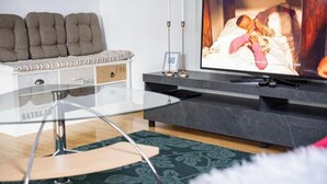 Ett modernt vardagsrum med ett soffbord i glas, en soffa med förvaringsutrymme, en platt-TV och en mönstrad matta.