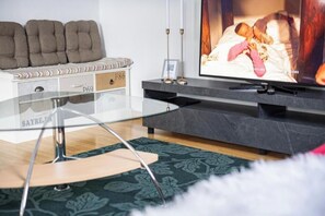 A modern living room with a glass coffee table, a sofa with storage, a flat-screen TV, and a patterned rug. - Flat at Border Suisse - Modern apartment with terrace near Basel (Saint-Louis)