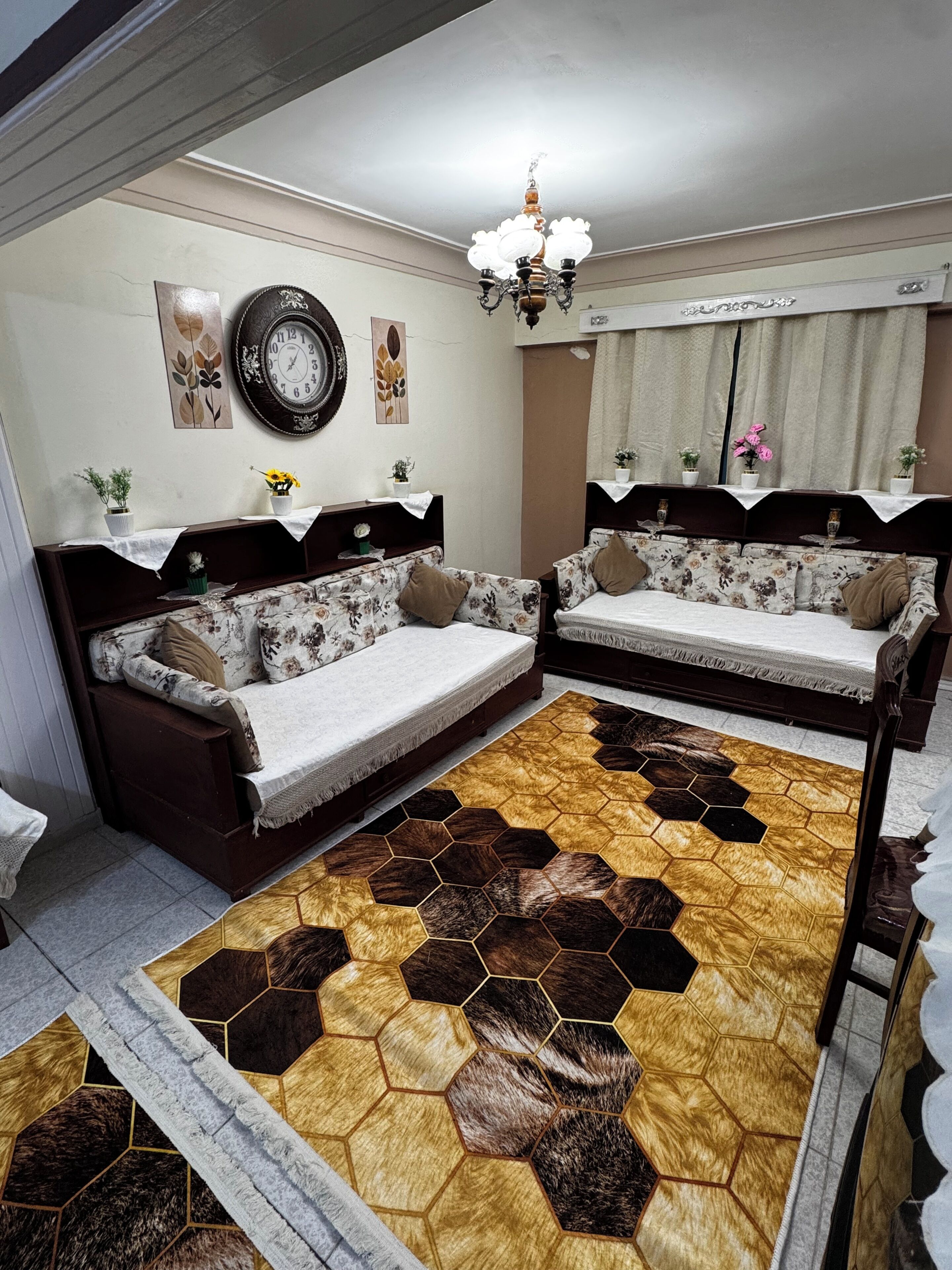 Ein Wohnzimmer mit zwei Sofas, einem gemusterten Teppich, einer Wanduhr und einem Kronleuchter.