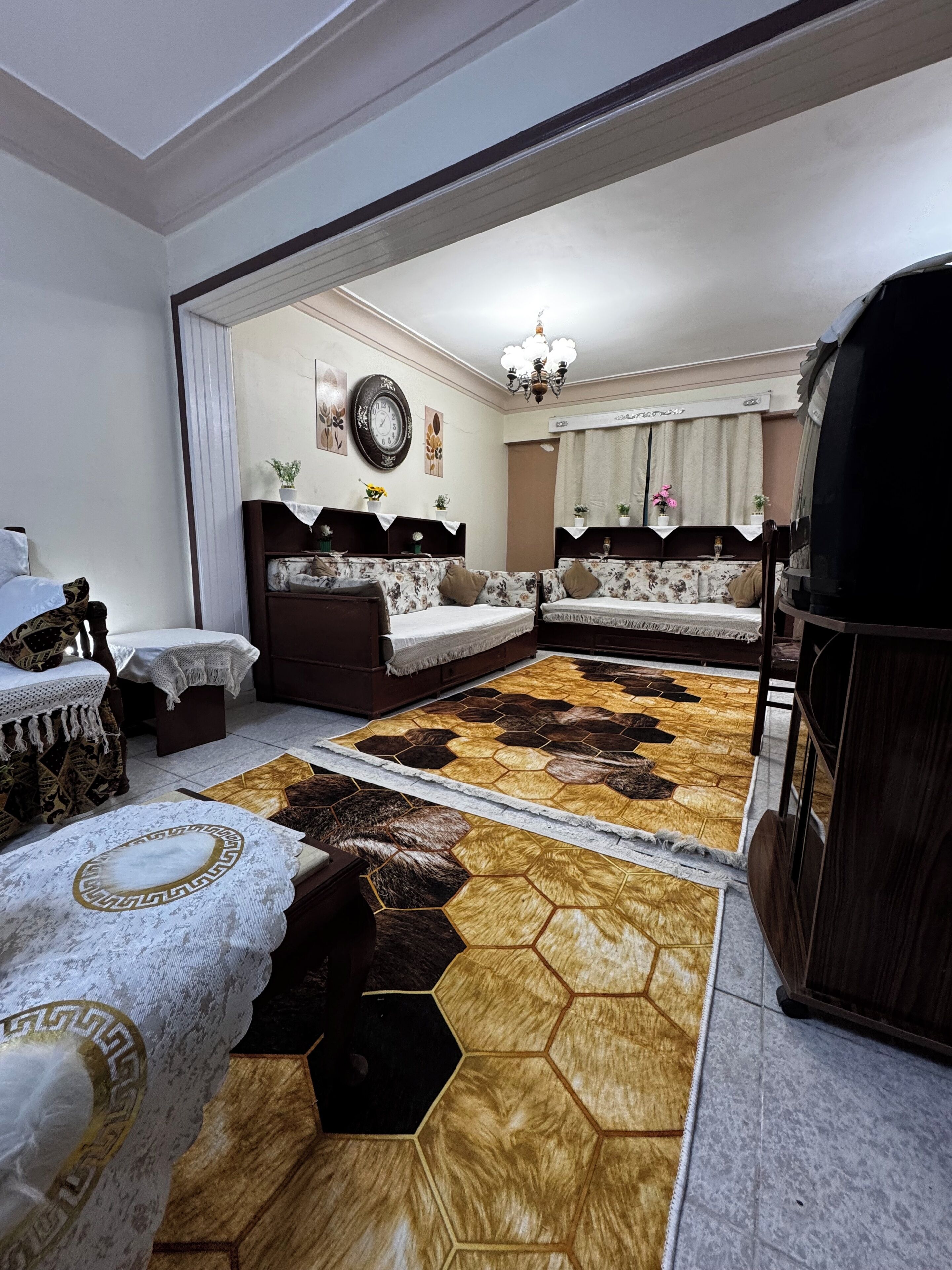 A room with a large mirror reflecting a bed, a sofa, and a rug with a geometric pattern.